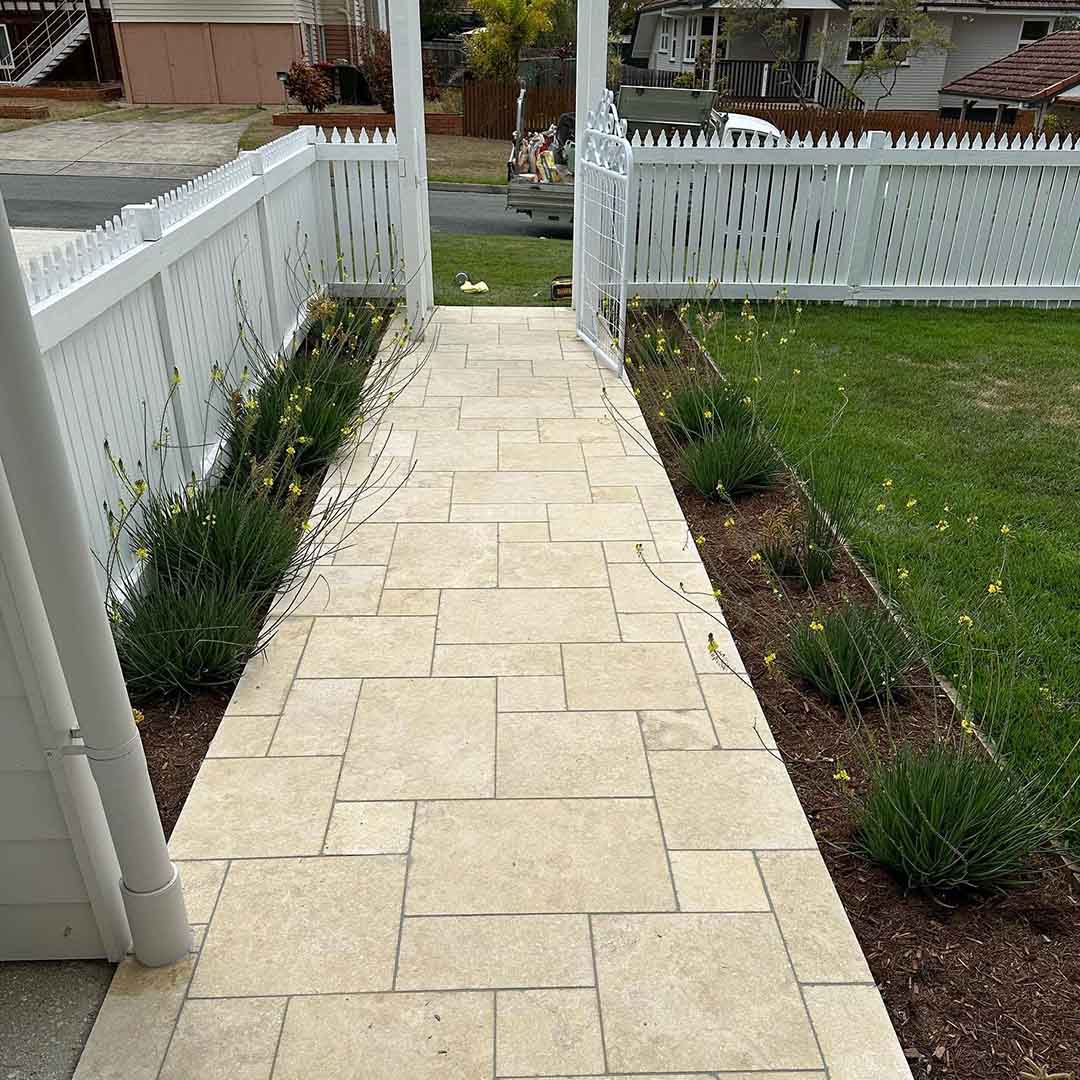 Pale stone paver path between a white picket fence and garden beds