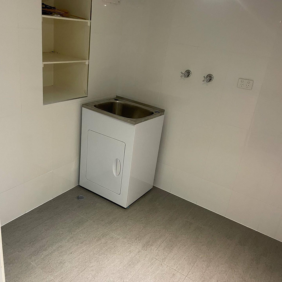 Laundry with white wall tiles, grey floor tiles and a laundry tub