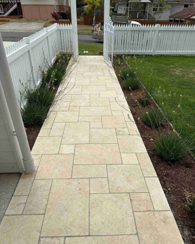 Pale stone paver path leading to a white picket gate, wider view