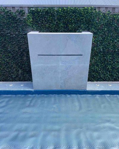 Close-up of a tiled water feature wall with a slot spout at a covered pool