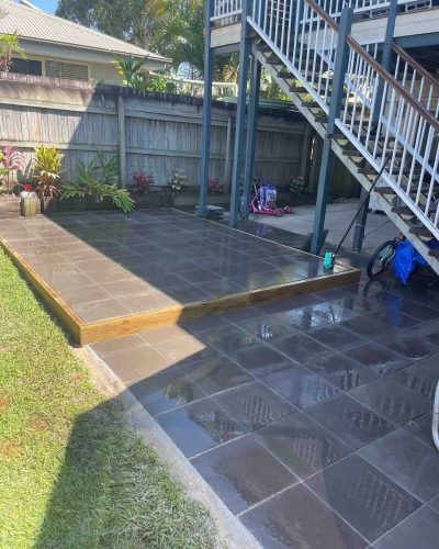 Dark grey tiled patio and step beside a lawn under outdoor stairs