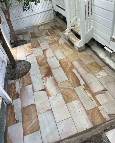 Sandstone-coloured pavers laid around trees at the foot of white stairs