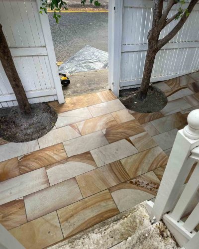 Close-up of sandstone-coloured pavers around two tree trunks by a white gate