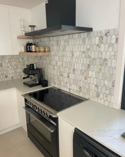 Kitchen with a marble-look oval mosaic splashback behind a black cooktop