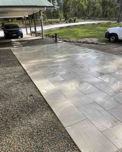 Pale paver path leading to a carport, edged with gravel