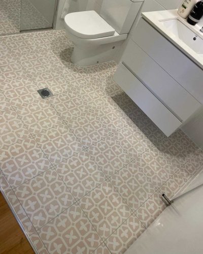 Patterned floor tiles around a toilet and wall-hung vanity in a bathroom