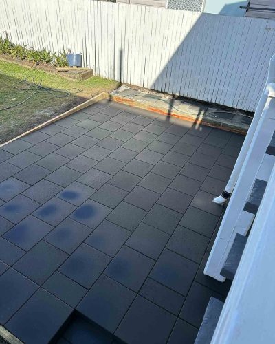 Dark grey pavers beside white stairs, with timber edging along the lawn